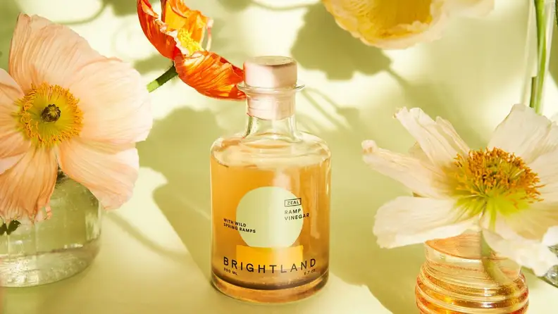 A bottle of Brightland's Zeal vinegar surrounded by spring flowers.