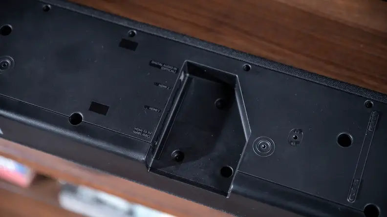 The black Q950a sits on a woodgrain cabinet with a cut-out for its inputs showing.