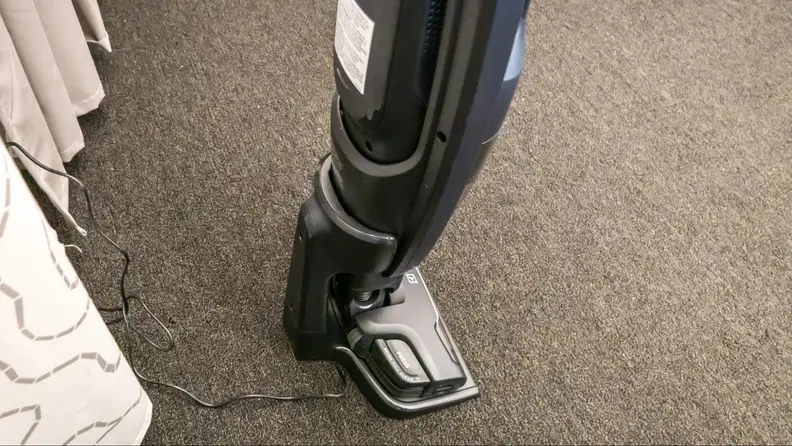 A cordless vacuum on brown carpet with its LED lights on.