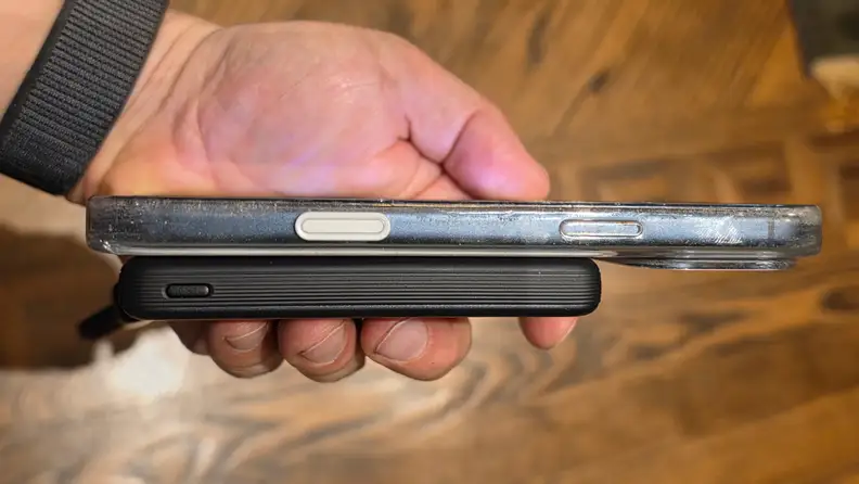 Side profile of iPhone shown with power bank attached held over a wooden surface.