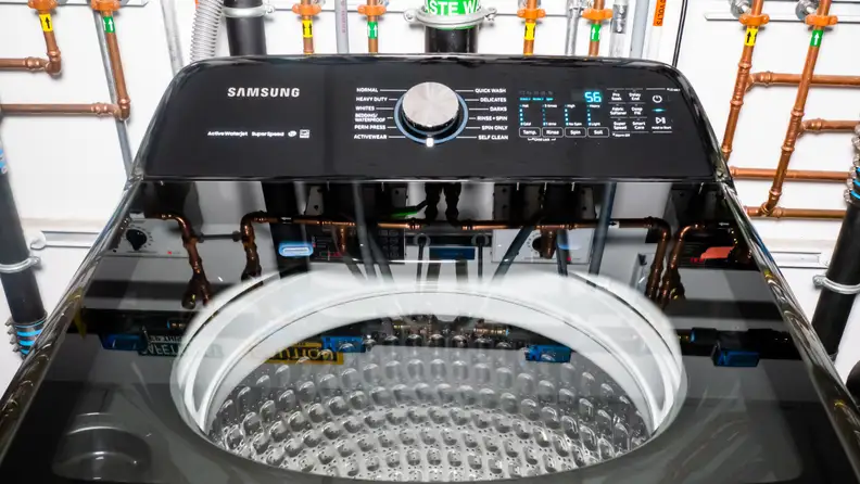 A shot of the top lid of the Samsung WA50R5400AV top-loading washing machine. In the background you can see the elaborate network of pipes we use to regulate water temperature and flow.