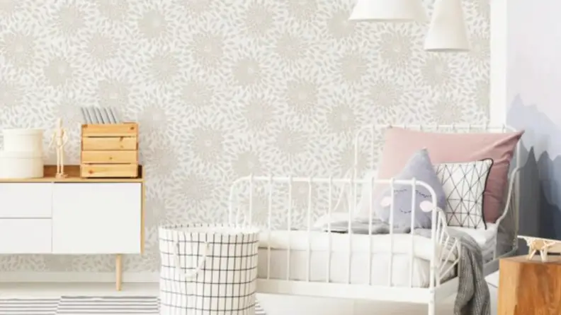 A beige floral design wallpaper in a room with a white dresser on the left and a white twin-sized bedroom on the right.