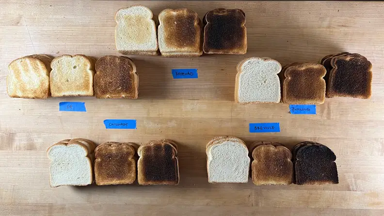 15 pieces of toast with varying browning laid out on a countertop with distinguishing labels from respective toaster brands.