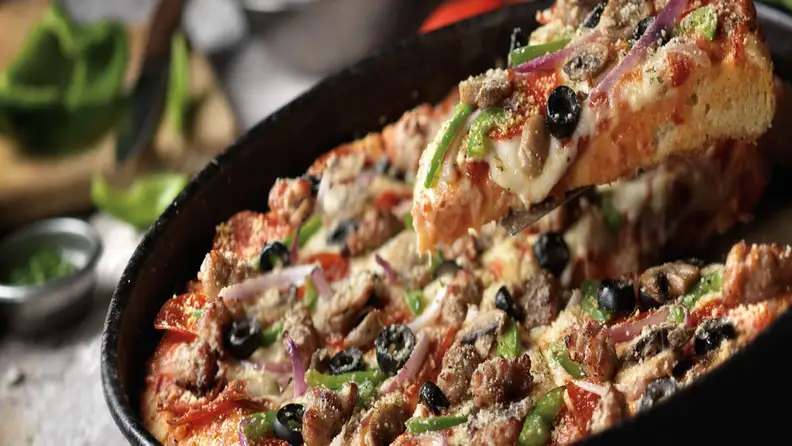 A slice of loaded pizza with olives, peppers, and sausage being lifted from the pan