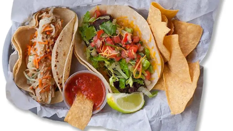 Two tacos and tortilla chips with salsa and lime
