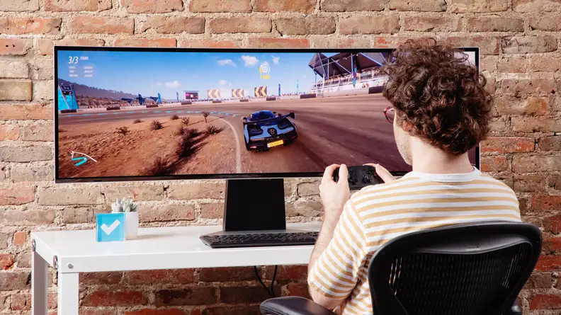 A person playing video games on the Samsung Odyssey OLED G9 on a brick background.