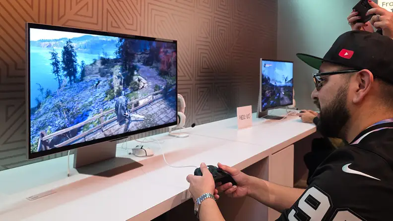 A gamer plays an action game on a Samsung 3D gaming monitor at a demo station, using a controller while the depth-enhanced display fills the screen.