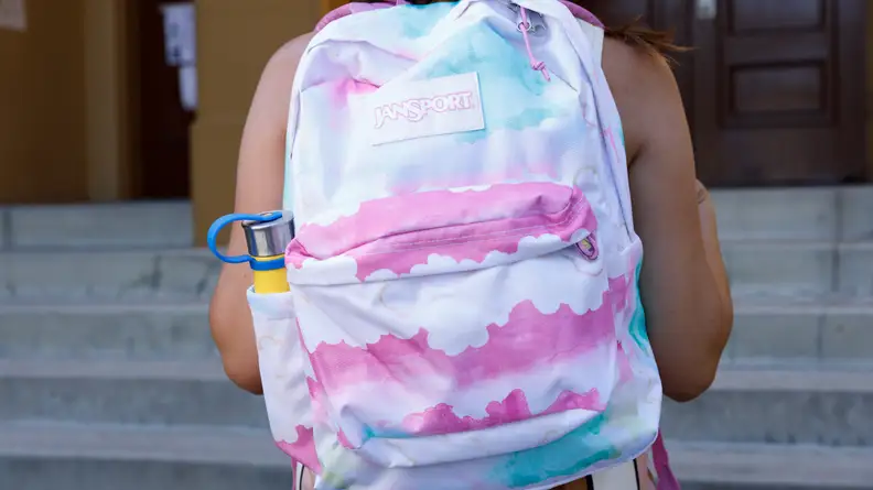 A child wearing a pink and white Jansport Superbreak Plus backpack.