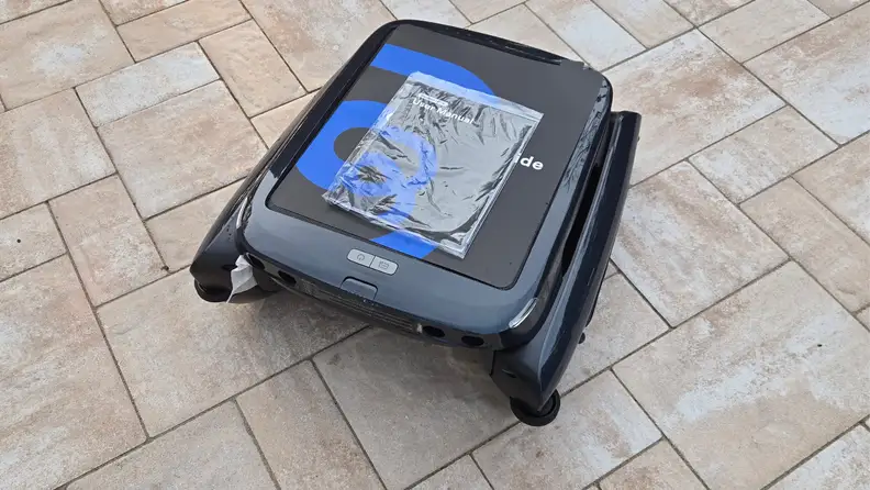 Black and blue Beatbot iSkim pool cleaner shown out of its box on a tan patio.