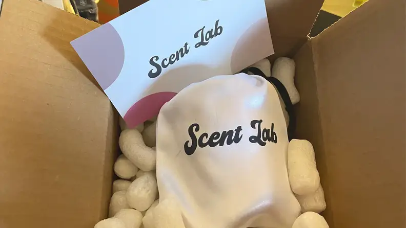 A white cloth bag with Scent Lab candle written in black on it, next to a Scent Lab Candle card inside a box.