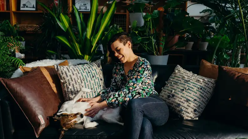 A woman pets her dog in a room of plants.