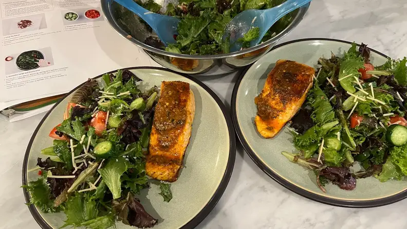 Two plates of salmon and salad next to salad bowl.