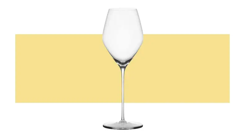 A single dessert wine glass on top a yellow background.