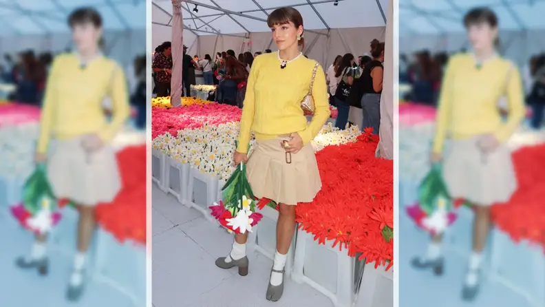 A woman wearing a yellow sweater and a khaki pleated skirt.