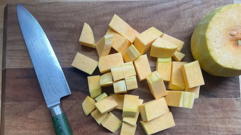 Hexclad's Damascus chef's knife with green handle next to pile of butternut squash cut in to cubes.