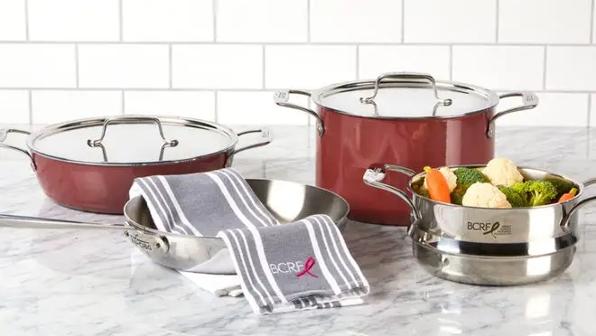 Silver and red pots and pans on stovetop, one with vegetables inside.