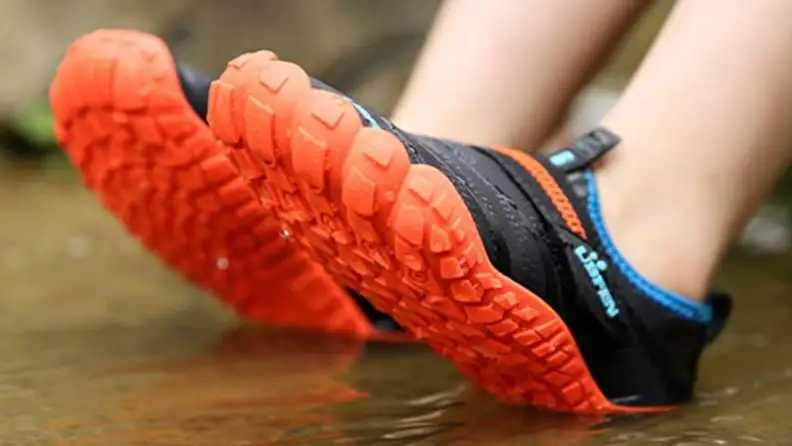 Orange soled water shoes on a child sitting in water.
