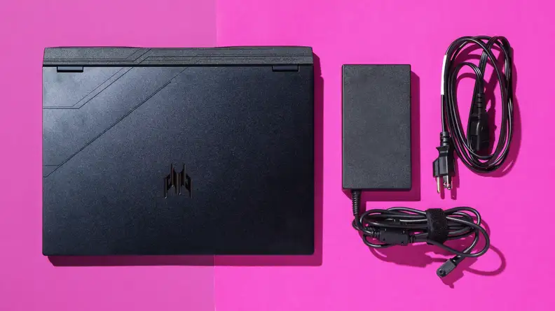 A black Acer Predator Helios Neo 14 gaming laptop with the power cable next to it, on a pink table