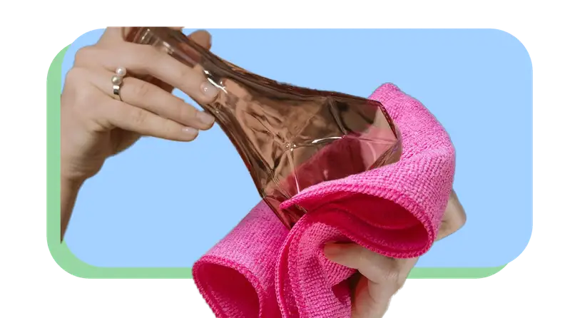 Person using pink microfiber cloth to clean off small glass colored vase