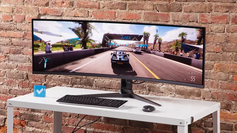 The Asus ROG Swift PG49WCD on a white table with a brick background.