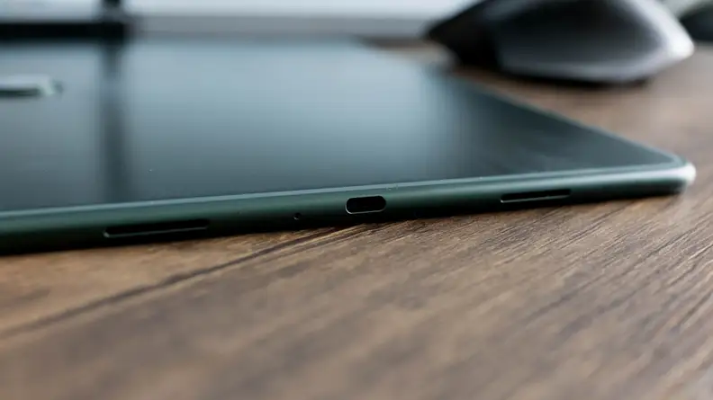 A tablet computer sits, face down on a table, it's charging port in view