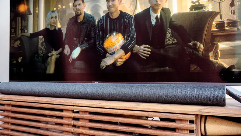 A black soundbar sits on a wooden TV console under a TV with Umbrella Academy playing.