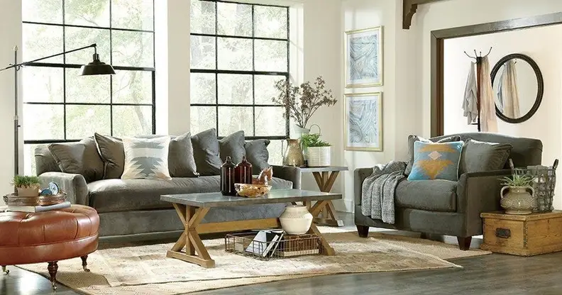 A sun drenched living room filled with two grey couches and a wooden coffee table.