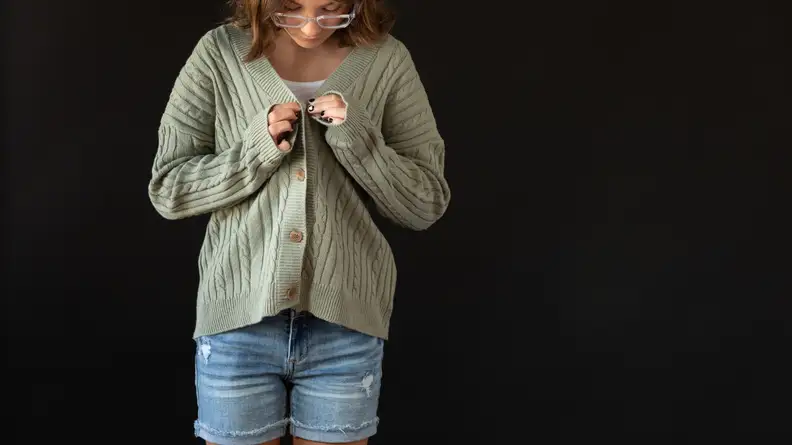 A tween buttons a green cardigan sweater.