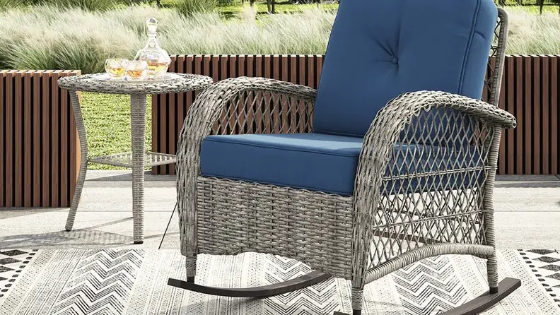 Wicker rocking chair with blue seat cushions outdoors.