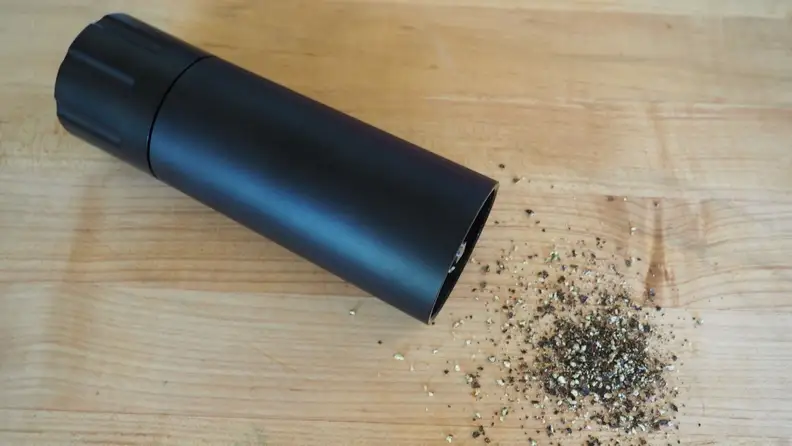 A black pepper grinder on a wood counter surrounded by ground pepper.