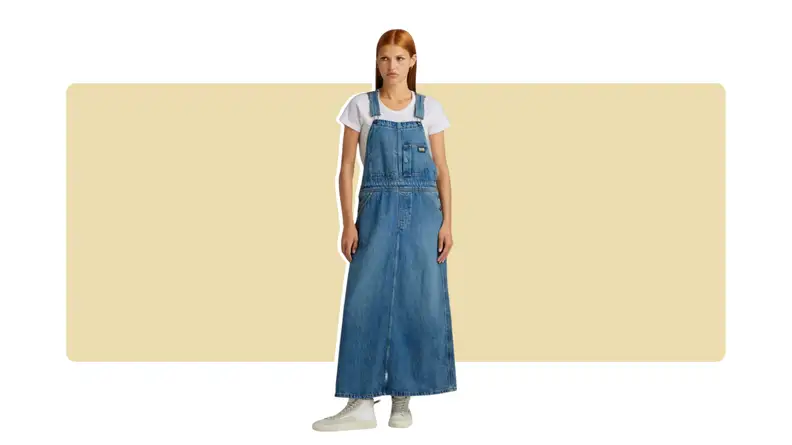 A model wearing denim skirt overalls with a white t-shirt.