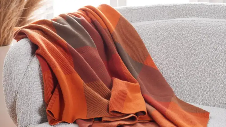 An image of an orange and deep red checked blanket draped over a sofa.