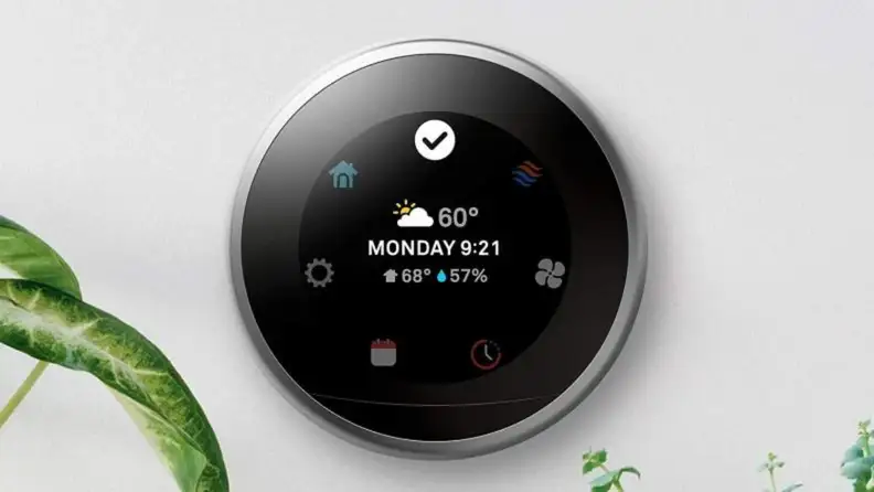 Smart thermometer with LED display mounted on wall next to indoor plant leaves.