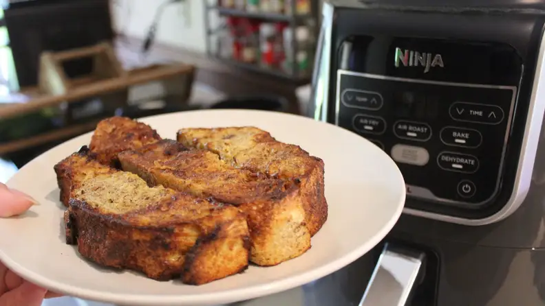 A plate of French toast sticks with the Ninja Air Fryer in the background