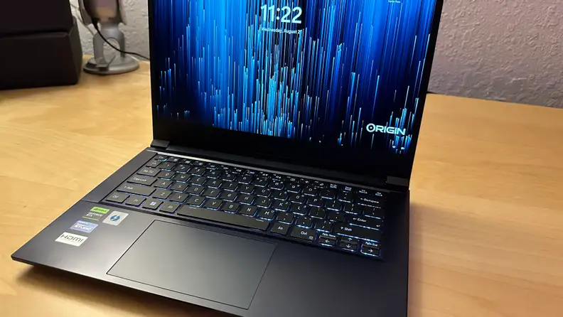 Origin EON14-S gaming laptop sitting on top of wooden surface with clock screen display turned on.