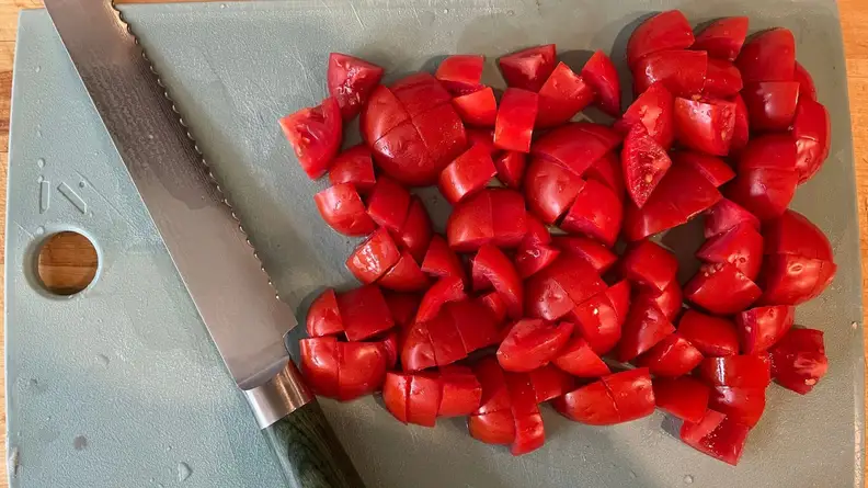 Jagged serrated knife from Hexclad's Damascus collection sitting next to pile of sliced tomatoes on top of gray cutting board.