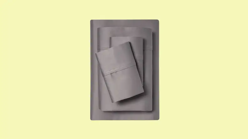 A stack of gray twin XL bed sheets sits on a pale yellow field