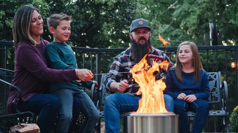A family of four grills hotdogs on a bonfire.