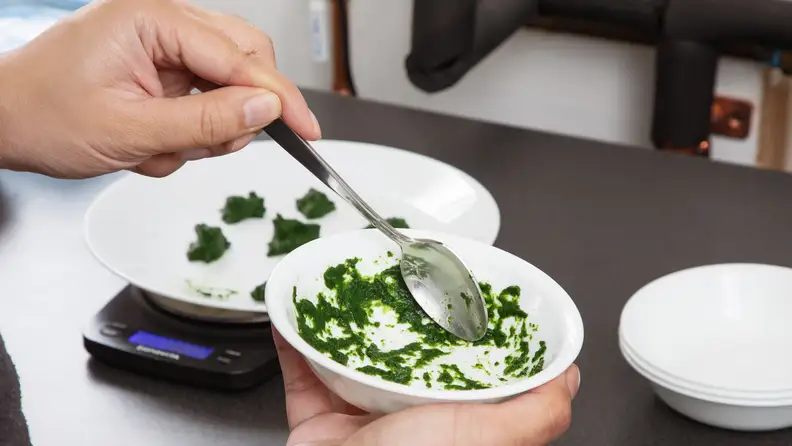 A hand moves a spoon around a dirty bowl, spreading a spinach stain around uniformly.