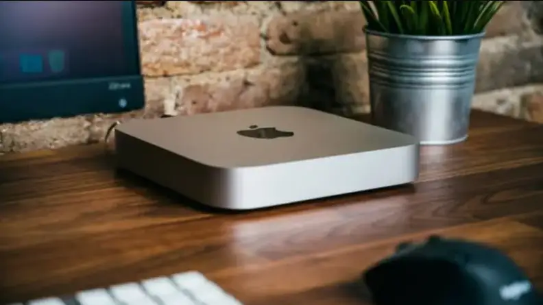 Apple TV product sitting on desk next to computer monitor.
