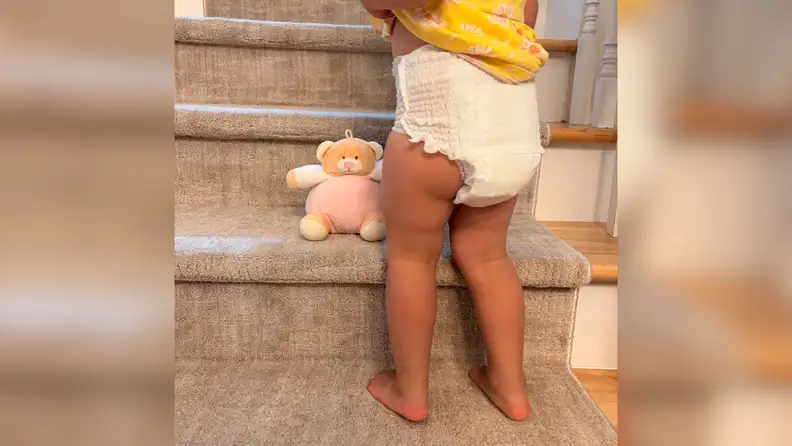 Baby girl standing in front of beige carpeted stairs wearing Coterie The 360 training underwear.