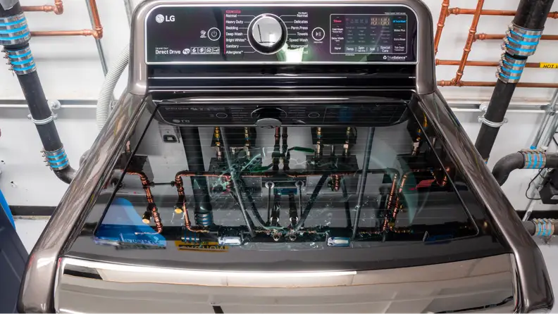 A close-up of the lid and control panel of the LG WT7900HBA top-load washing machine against a pipe-lined wall of our laundry testing lab.