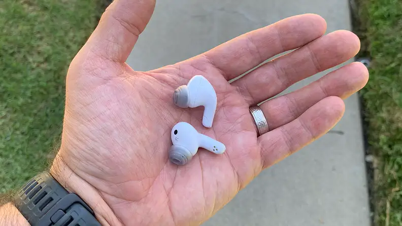 The LG T90Q earbuds in a man's hand with a walkway and grass in the background.