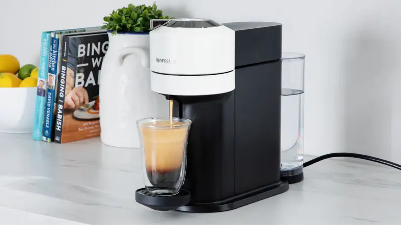 Nespresso Vertuo Next coffee maker on marble countertop next to potted plant and kitchen utensils.