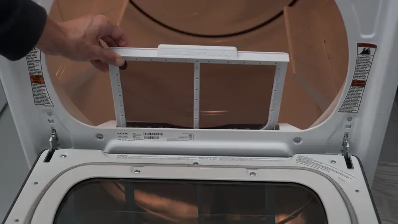A hand reaches into frame, pulling up the lint trap slightly.