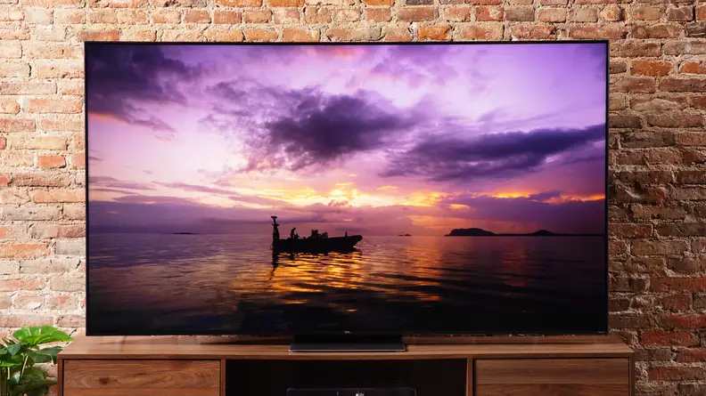 TCL 6-Series television in front of brick wall on top of wooden surface.