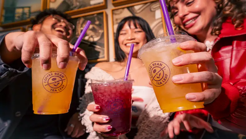 Three friends holding colorful iced drinks with purple straws