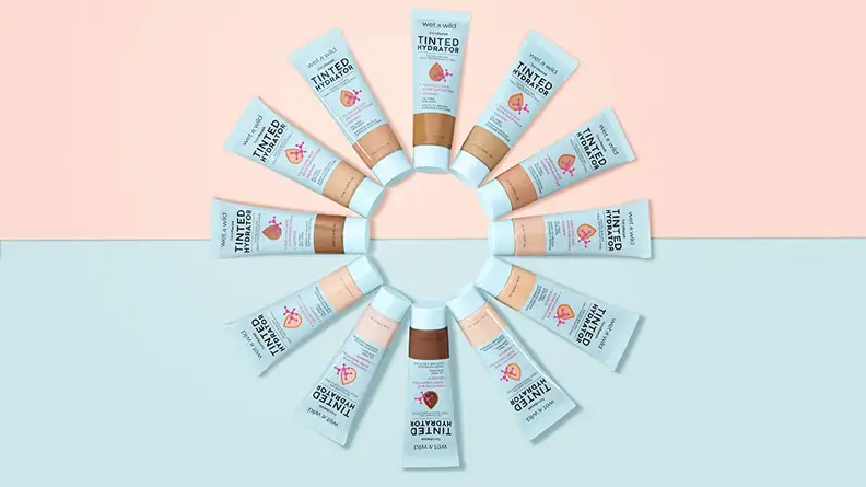 A circle of 12 Wet n Wild Bare Focus Tinted Hydrators on a blue and pink background.