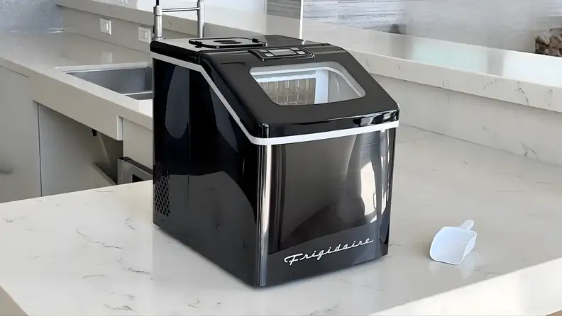 Frigidaire EFIC452 clear ice maker sitting on a kitchen countertop next to a plastic ice scoop.