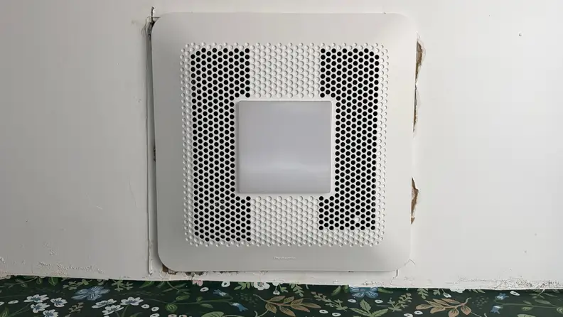 An exhaust fan on a ceiling next to a green floral wall